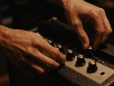 Close-up of hands adjusting vintage amplifier knobs, warm tungsten glow, deep shadows, 35mm film grain
