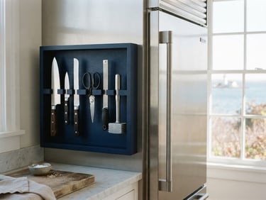 Bright natural coastal daylight illuminating neatly organized professional tools next to a high-end stainless steel refrigerator door, crisp editorial photography