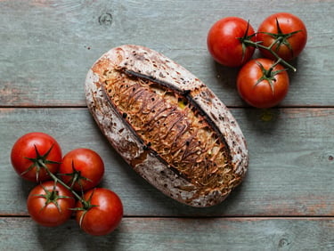 Overhead flat-lay of a rustic wooden table with fresh sourdough bread, heirloom tomatoes, and olive oil, soft Scandinavian daylight.