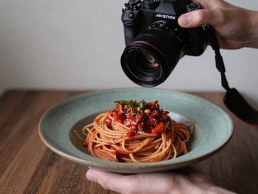 A hand holding a high-end camera over a beautifully styled rustic plate of pasta, behind-the-scenes content creation.
