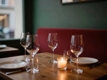 A cozy restaurant interior at dusk, warm candle glow on empty wine glasses, soft focus, intimate atmospheric lighting.
