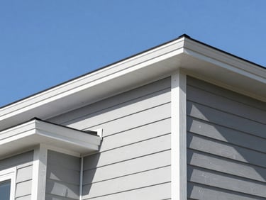 Crisp architectural photograph of newly installed light-grey vertical siding and clean rooflines against a clear blue sky, bright daylight.