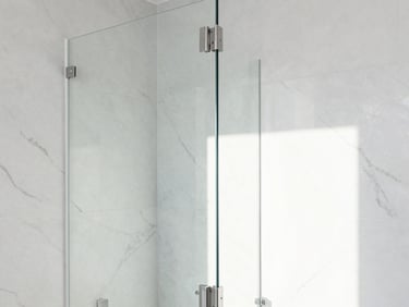 Bright architectural detail of a newly remodeled luxury bathroom, white marble tiles, clean glass door, bright natural daylight