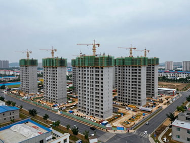Wide exterior of a large mixed residential development site showing active construction progress, surrounding infrastructure and access roads visible, overcast daylight, no people