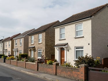 Wide exterior of a compact two-storey residential row-house complex, garden boundary wall in foreground, overcast natural daylight, quiet residential street context, no models