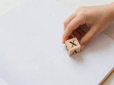 Overhead flatlay of a printed workbook page with a child's hand placing a small wooden block on a letter, soft diffused light