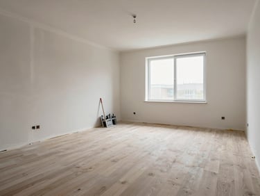 Freshly finished room interior after restoration turnover, new drywall painted, clean flooring installed, daylight through bare window, no furniture, construction tools staged neatly against the far wall