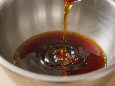 Pouring dark rich liquid seasoning into a stainless steel mixing bowl, macro shot