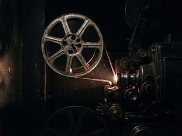 Dark cinematic film photography of a vintage 35mm film projector reel, glowing dust particles in a dark projection booth, high-contrast chiaroscuro lighting, deep shadows.