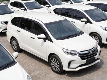 Barisan mobil MPV putih bersih seperti Avanza dan Xenia terparkir sejajar di area parkir terbuka yang luas, pencahayaan alami siang hari.