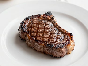 Close-up of a perfectly seared ribeye steak, juicy and tender, with a crisp crust, served on a minimalist plate in an elegant setting, bright natural daylight, soft shadows.