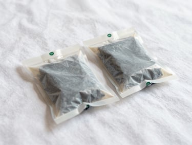 Two folded compression packing cubes sitting on a clean white bedsheet, bright daylight, realistic saturated tones, 35mm lens