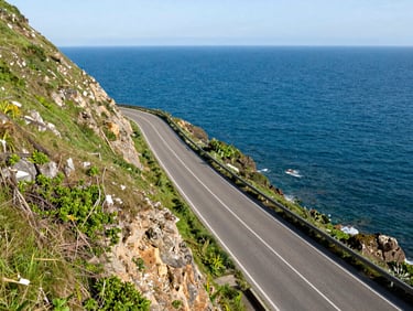 Crisp aerial view of a clean asphalt road winding along a dramatic coastal cliff under bright daylight, no cars, sharp ocean horizon.