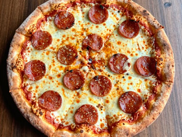 Close-up of a sizzling Neapolitan pepperoni pizza, pepperoni cups charred at the edges, bubbling cheese, warm firelight.