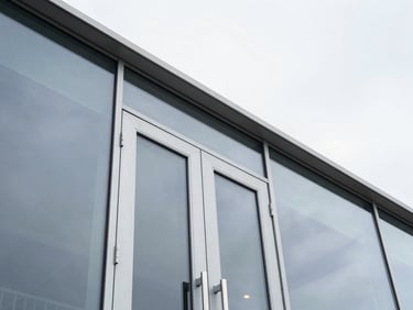 Low-angle architectural shot of a modern glass facade with a sleek aluminum sliding door installed, bright natural overcast daylight, cool metallic tones, sharp focus.