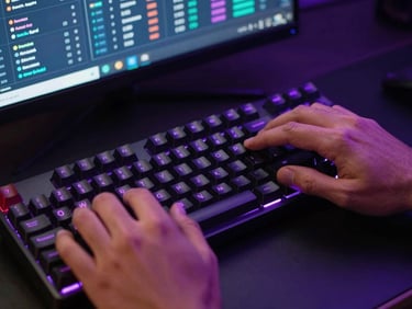 Close-up overhead of hands on a mechanical keyboard in a dark gaming setup, neon violet light reflecting off keycaps, a search analytics dashboard visible on screen in background, high-contrast broadcast lighting