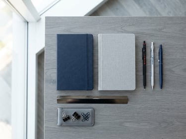 Clean flat-lay of modern office stationery, organized blue and gray notebooks, architectural pens, bright natural window light, professional depth of field