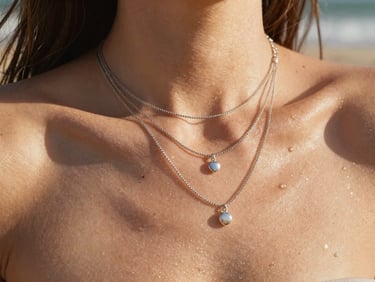 Layered silver necklaces on skin glistening with seawater, bright direct sunlight, beach background