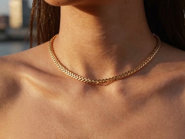 Sleek gold herringbone chain on a woman's collarbone, warm dusk lighting, city reflections