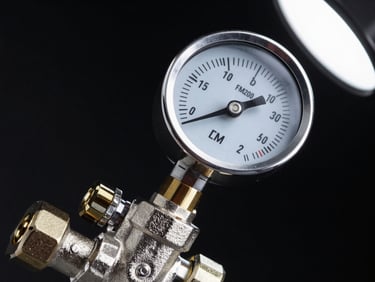 Macro close-up of an FM200 cylinder valve head and pressure gauge, polished steel body, cool studio strobe from upper right casting sharp shadows, black background