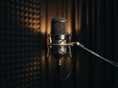 Moody editorial photograph of a high-end vintage condenser microphone inside a dark soundproof booth, warm amber backlight catching the metallic mesh, shallow depth of field, 35mm film grain.