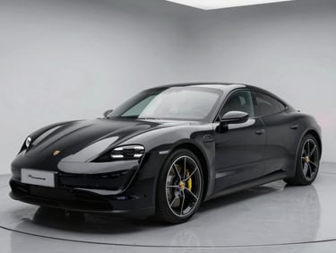 Sleek black Porsche Taycan electric sedan parked in a modern showroom with overhead studio lighting.