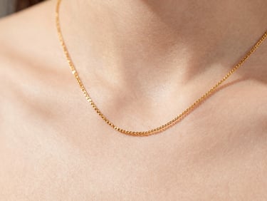 Macro detail of an uninterrupted gold necklace draped elegantly on skin, soft daylight, high-key editorial jewelry photography, shallow depth of field.