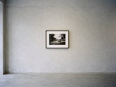 A quiet minimalist gallery space with soft natural light, empty concrete walls, single framed black and white photography on the wall, medium format film, clean composition