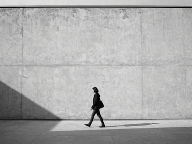 A lone figure walking past a massive minimalist concrete wall in Ankara, sharp shadows, soft natural light, medium format black and white photography.