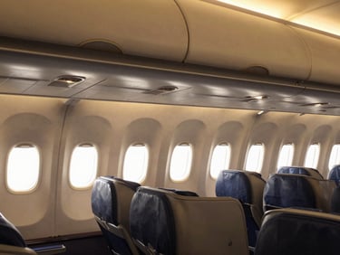 Clean, luxurious airplane cabin interior, empty, with golden hour light streaming through the windows, wide-angle environmental framing, premium travel photography