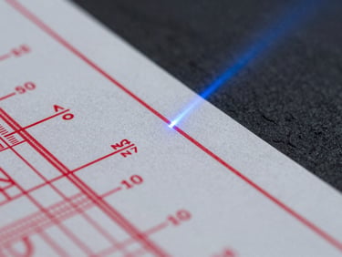 Extreme close-up of a heavily redacted physical document with technical schematics, sharp clinical light, dark slate background, high contrast, sterile, 35mm