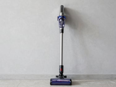 A premium cordless vacuum cleaner standing against a neutral grey kitchen wall, natural daylight, crisp details.