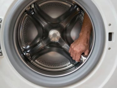 Close-up of hands pulling laundry drum forward inside a washing machine, clean work-light illumination, stainless drum detail visible
