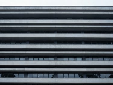 Symmetrical eye-level shot of a modern civic building facade with clean horizontal lines, cool diffused overcast daylight, desaturated navy and gray tones.