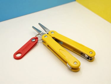 Bright high-key product photography of a modern yellow multi-tool and red keychains on a crisp off-white background, studio light, sharp focus
