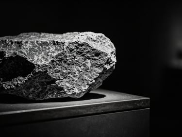 Stark monochrome gallery photography, close-up of physical textures, raw stone balanced precariously on a bronze edge, dramatic spotlighting against absolute black, 35mm