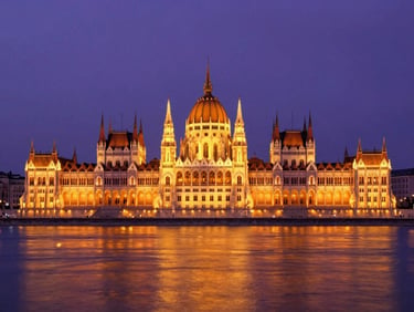 Dramatic wide-angle view of the Hungarian Parliament building in Budapest at twilight, glowing orange lights reflecting on the Danube river, deep purple sky