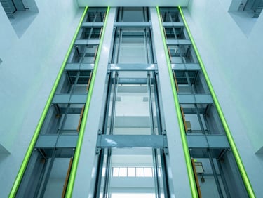 Wide-angle architectural perspective of a massive high-capacity freight lift bay, clean geometric symmetry, bright high-key interior lighting with cool blue tones and sharp neon green light paths