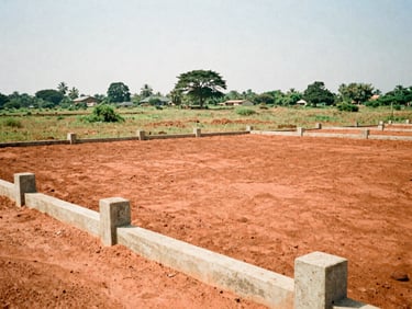 Cleared flat red earth plot in Abeokuta Ogun State, concrete boundary pillars, sunny afternoon, 35mm film
