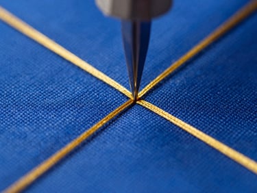 Extreme macro close-up of a high-speed embroidery needle piercing deep royal blue heavy canvas fabric, gold thread creating a crisp geometric pattern, bright directional studio lighting, shallow depth of field