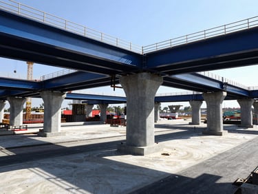 Wide environmental shot of a major civil infrastructure project, highway bridge piers under construction, high contrast daylight, sharp shadows