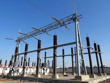 High-voltage electrical substation with steel gantry structures against a crisp blue sky, sharp shadows, daylight