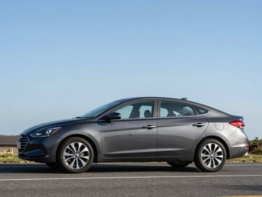 Three-quarter exterior shot of a dark grey Hyundai Elantra on an open Cayman road in daylight, full vehicle profile, road and sky visible in background