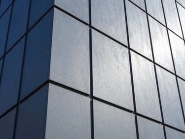 Close-up of a high-performance architectural material facade, showing texture and weather resistance, crisp daylight, cool blue and steel gray tones, high-contrast architectural photography.