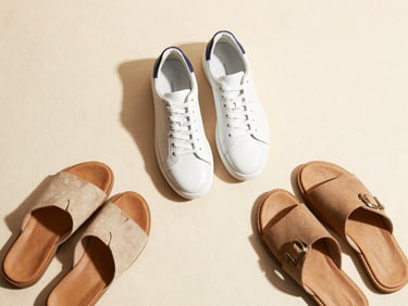 Clean minimalist flat lay of modern leather sneakers and casual sandals on a neutral background, warm natural light
