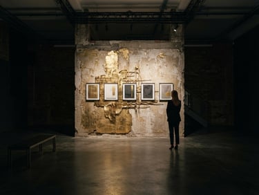 A wide panoramic editorial photograph of a minimalist Shoreditch gallery space, dramatic chiaroscuro lighting, deep rich shadows, gold accents on a single raw textured wall.