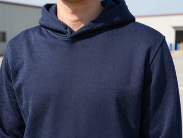 Close-up of a men's navy blue heavy-knit cotton hoodie texture, showing clean flatlock seams, bright natural daylight, 35mm
