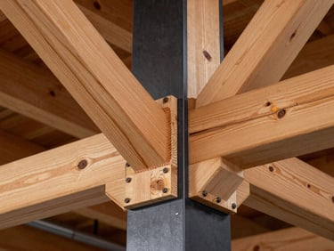 A close-up of heavy-duty steel-to-timber joinery, showcasing warm exposed cedar trusses bolted into a matte black steel column