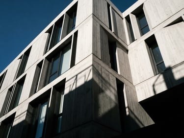 High-contrast architectural angle of a minimalist concrete building facade, sharp direct sunlight, deep geometric shadows, 35mm lens