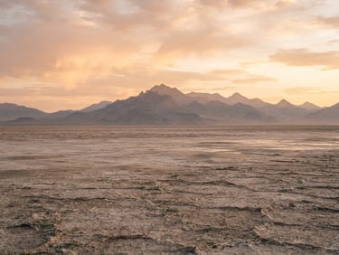 Sweeping natural vista of Utah's salt flats and distant mountain ranges at golden hour, soft diffused light, wide environmental shot, warm editorial photography.